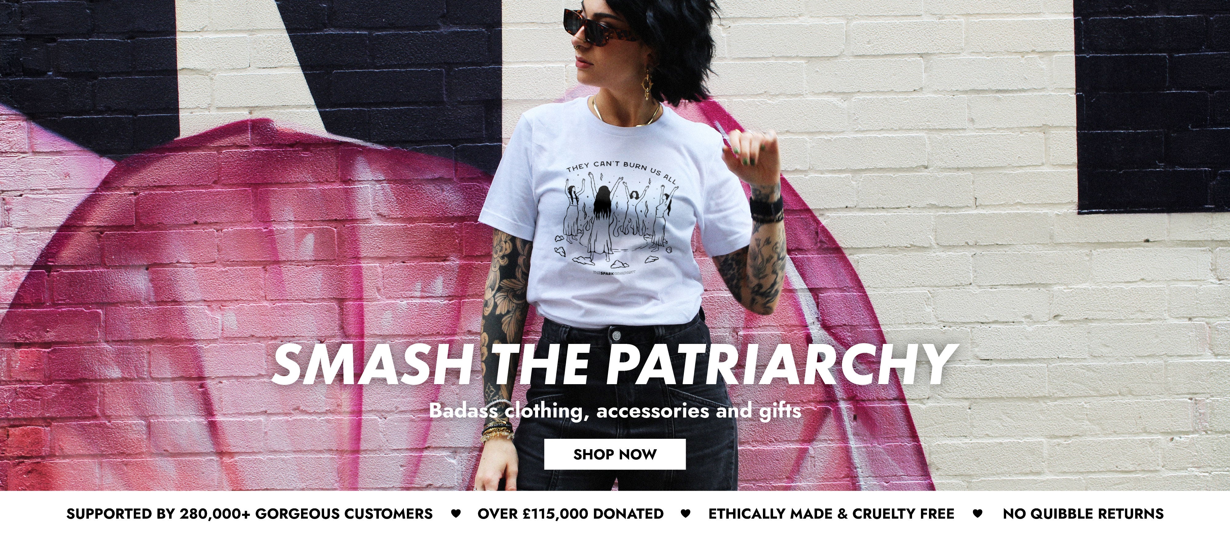 Woman wearing a t-shirt with 'Smash the Patriarchy' text, standing in front of a mural.