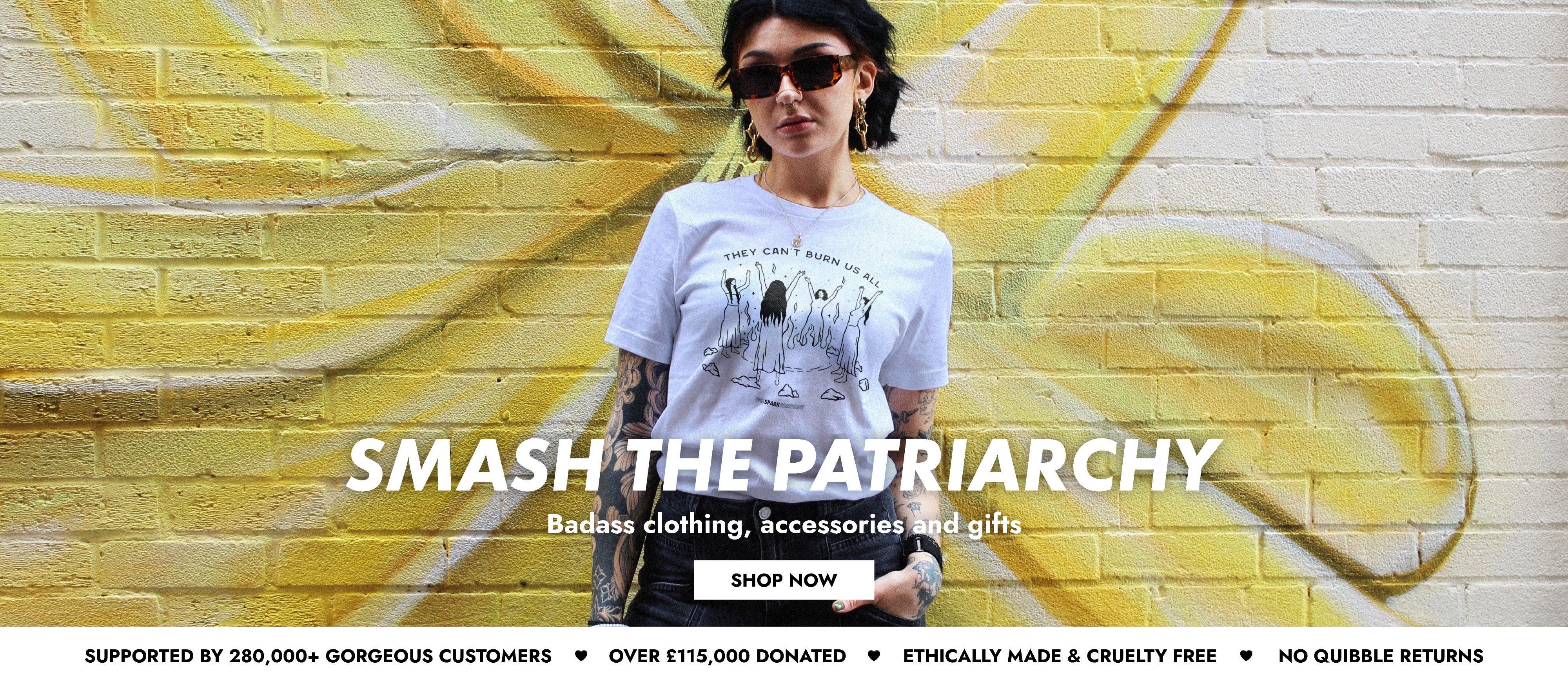 Woman wearing a t-shirt with 'Smash the Patriarchy' text in front of a yellow and white mural.